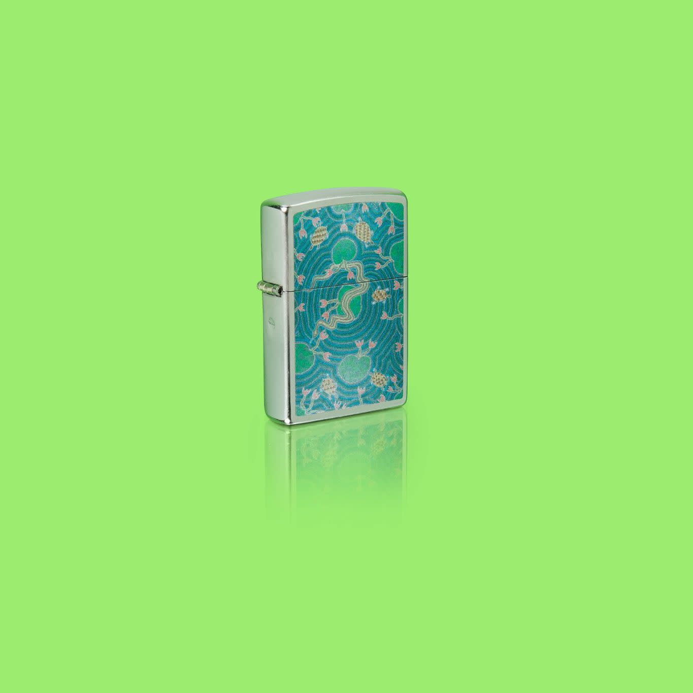 Glamour shot of Zippo John Smith Gumbula Snake & Turple Design Street Chrome Windproof Lighter standing in a green scene.